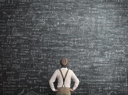 young man stares up at a chalkboard that is covered in mathematics