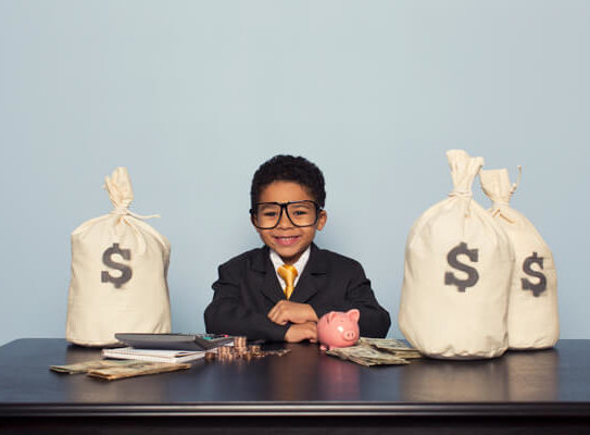 young boy in business clothes sitting at a desk with a bunch of money