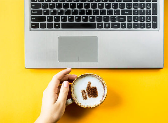 cup of coffee in front of a laptop and in the cup of coffee is the shape of a thumbs up