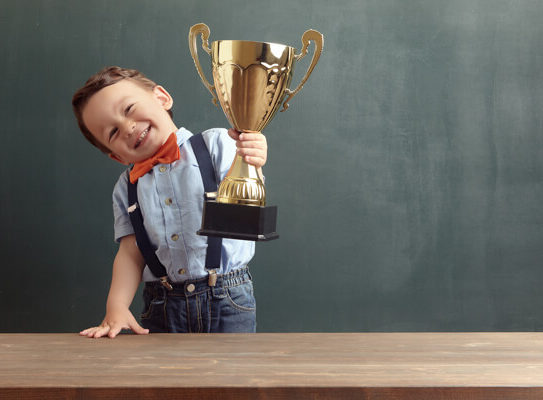 young boy in business clothing holding a trophy