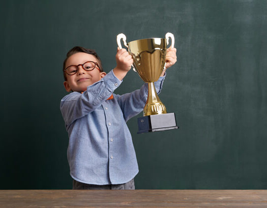 young boy in business clothing holding a trophy