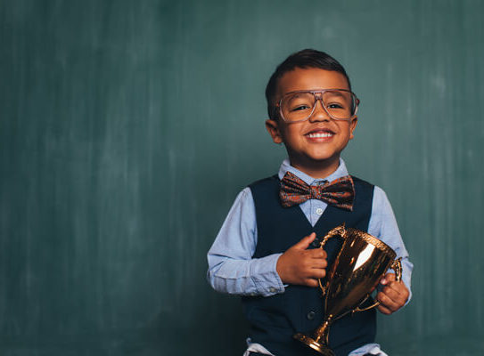 young boy in business clothing holding a trophy