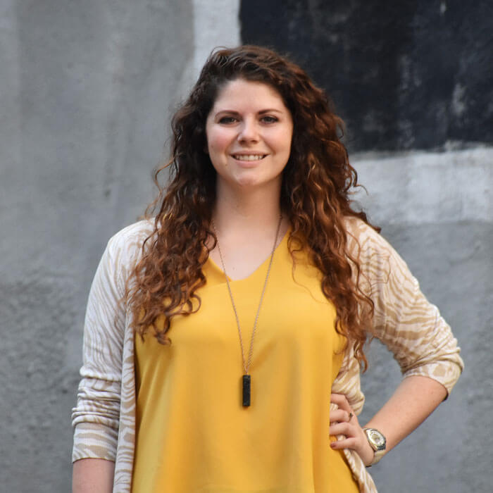 Heather Waldron smiling and standing in front of grey cement wall