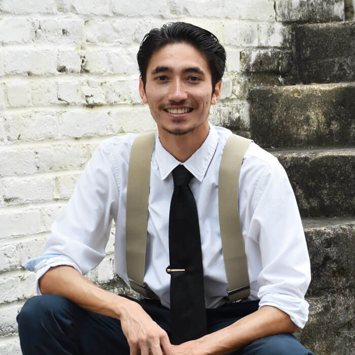 John Ryan Lechner smiling and sitting on a brick staircase. He needs a haircut and to tuck in his shirt in the back more