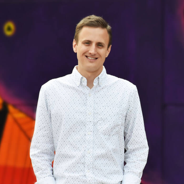 Matthew Michael smiling and standing in front of colorful mural