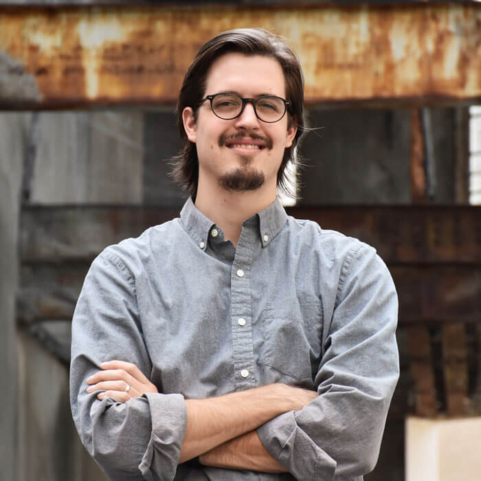 Matt Thielke smiling and standing in front of industrial background