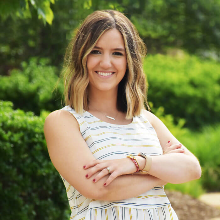 Taylor Chamberland smiling and standing in front of bushes