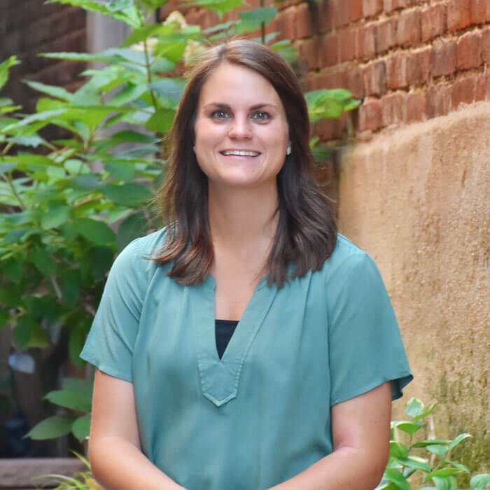 Tracie Davis smiling and sitting in courtyard with greenery