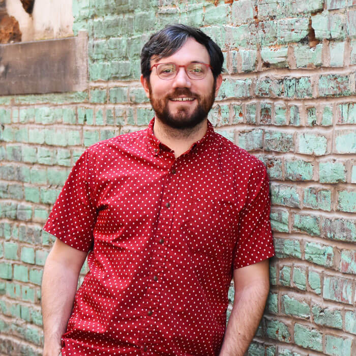 Will Hawthorne smiling and leaning against turquoise brick wall