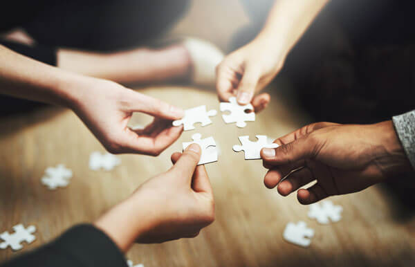 4 puzzle pieces, each being held by a person sitting on the floor