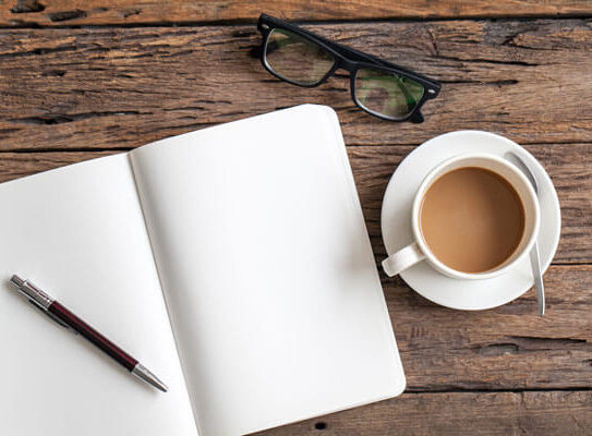 blank notebook on a wooden table next to a pair of glasses and a coffee cup