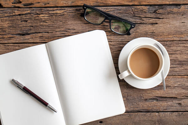 blank notebook on a wooden table next to a pair of glasses and a coffee cup