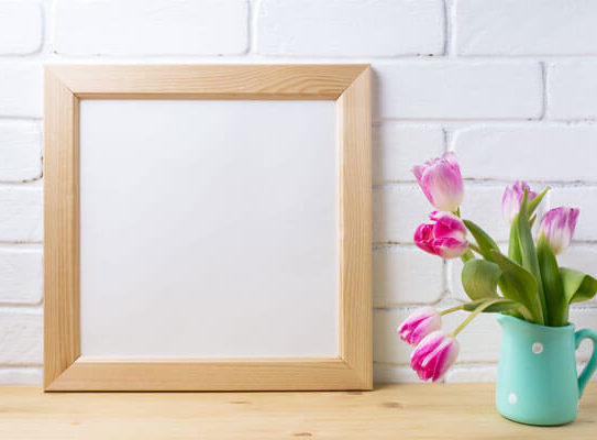 blank picture frame sitting next to a cup with flowers in it