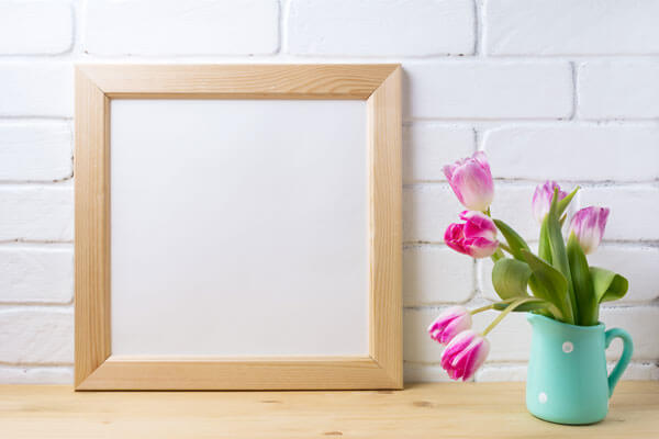 blank picture frame sitting next to a cup with flowers in it