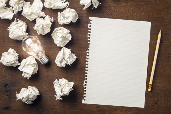 crumpled pieces of paper are sitting on a table next to a clean sheet of paper and a lightbulb
