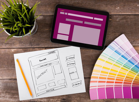 a mockup design, color swatch booklet, and tablet are placed on a table next to a plant