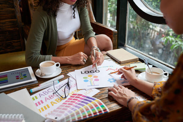 two women sit at a table and discuss color watches and logo designs