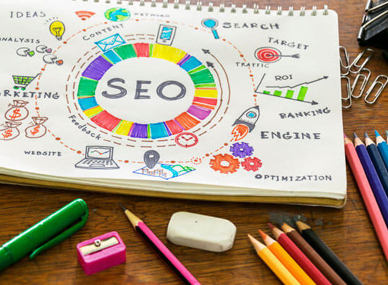 a drawing of several aspects of search engine optimization is on a wooden table with colored pencils, and paper clips