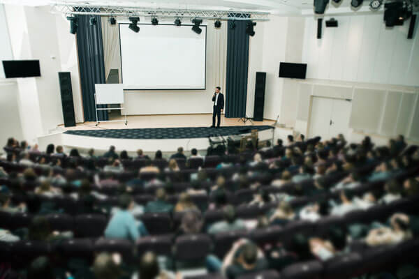 a young man is standing on a stage and speaking with a microphone in front of a crowd