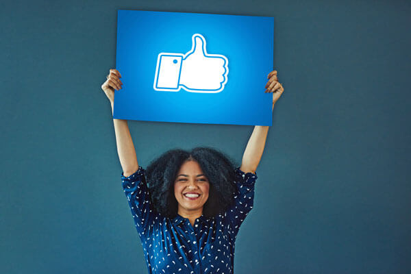 smiling young woman triumphantly holds a sign above her head that has a 'thumbs up' icon on it