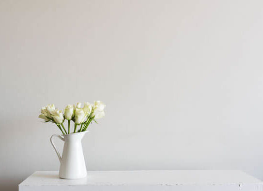 white flowers sitting in a white jug on a white table with a white background
