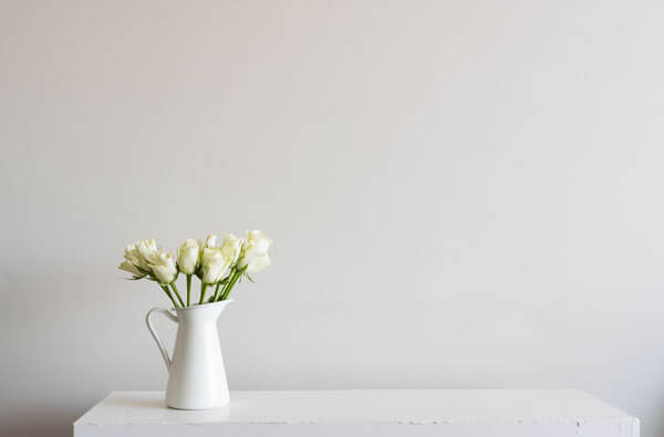 white flowers sitting in a white jug on a white table with a white background