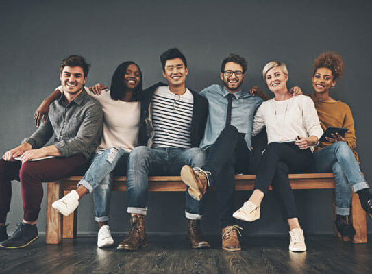 group of happy young adults sit on a bench together