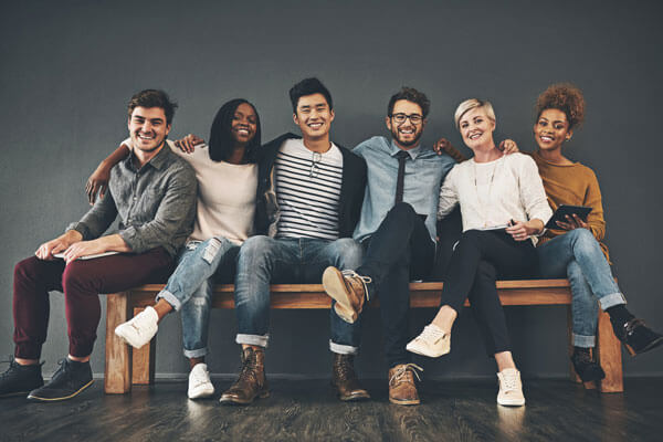group of happy young adults sit on a bench together