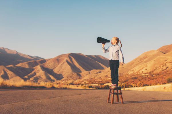 young girl standing on a stool with a megaphone in a mountainous desert