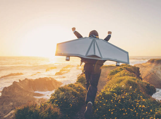 a young man running into the sunset with his arms raised and wearing a cardboard jetback