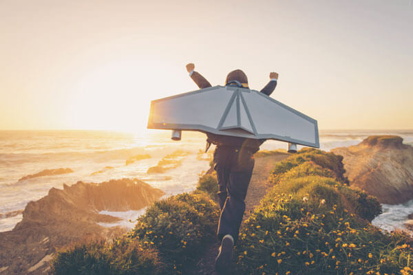 a young man running into the sunset with his arms raised and wearing a cardboard jetback