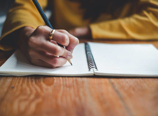 a closeup shop of a hand writing in a notebook with a pencil