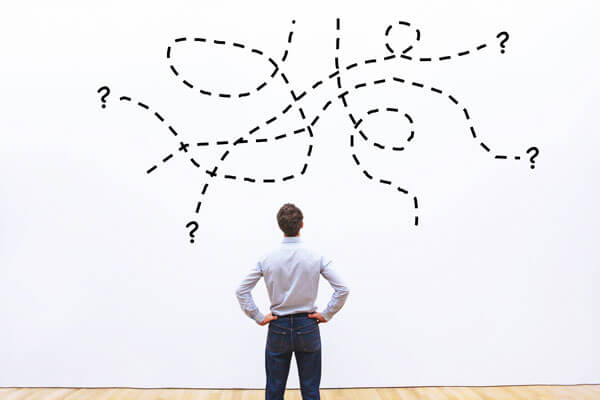 young man stares at a wall with several intersecting dotted lines and question marks painted on it