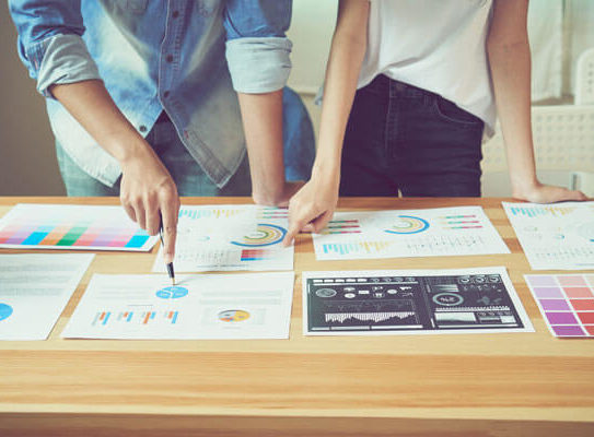 two women analyze charts and color swatches on a table