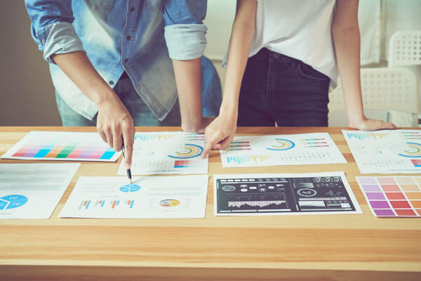 two women analyze charts and color swatches on a table