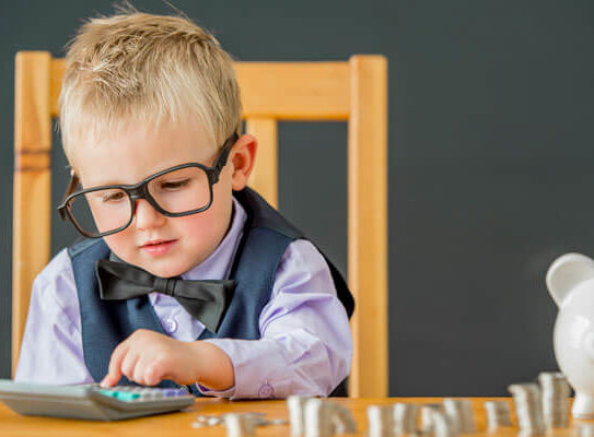young boy in a vest and bowtie is using a calculator to count his piggy bank money