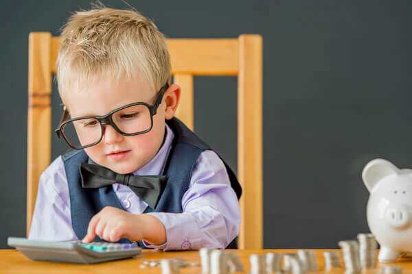 young boy in a vest and bowtie is using a calculator to count his piggy bank money