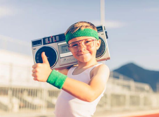 smiling young boy holding a boombox and giving a thumbs up