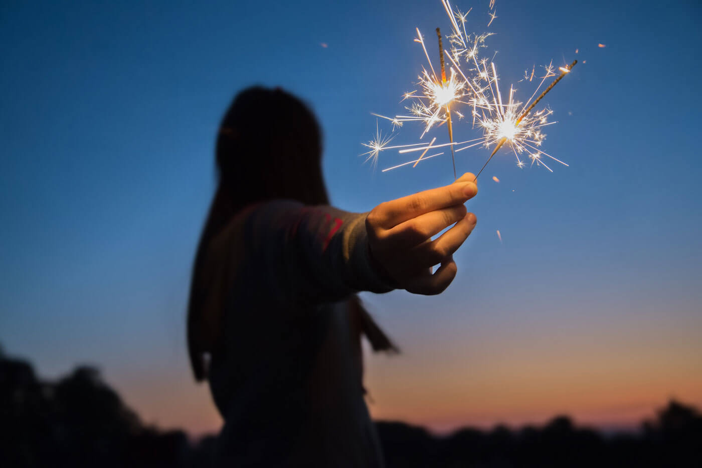 young girl holds two sparkling fireworks at night