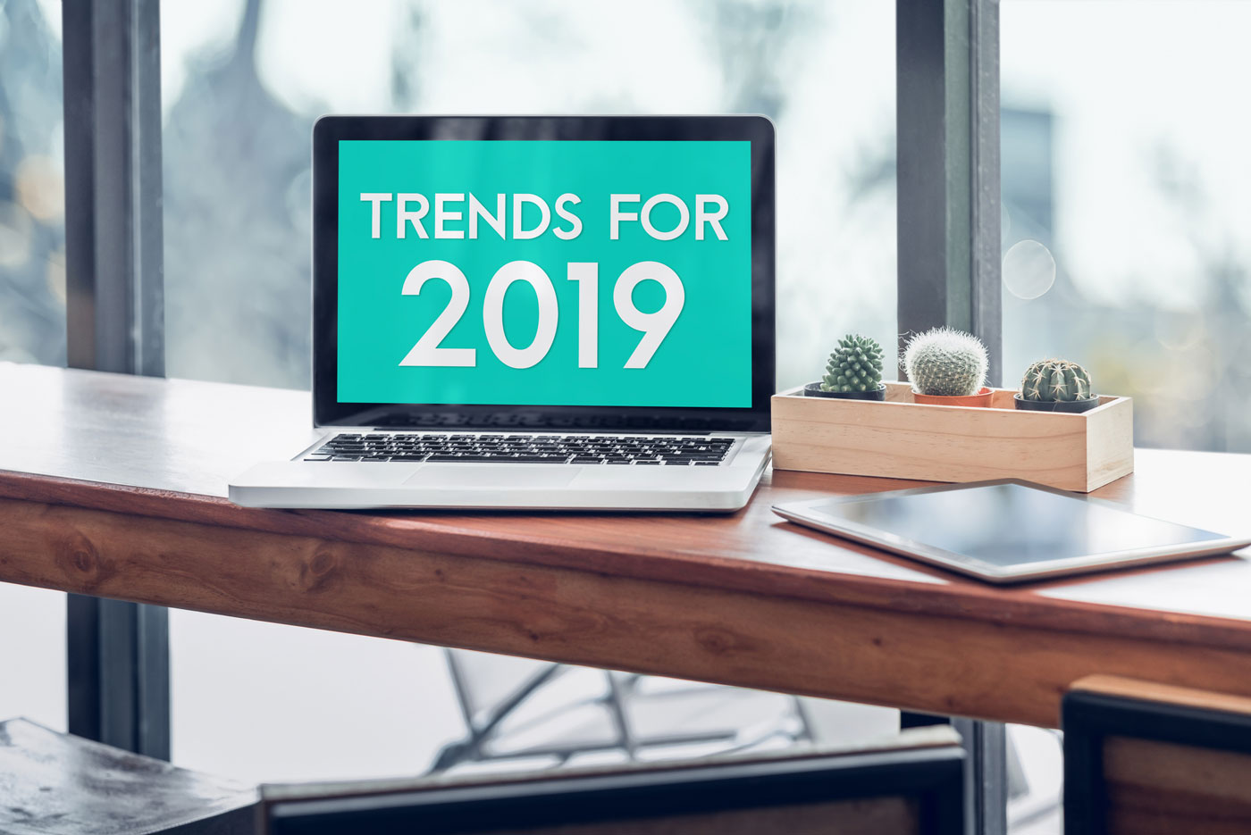 Trends for 2019 word in laptop computer screen with tablet on wood stood table in at window with blur background,Digital Business or marketing trending.