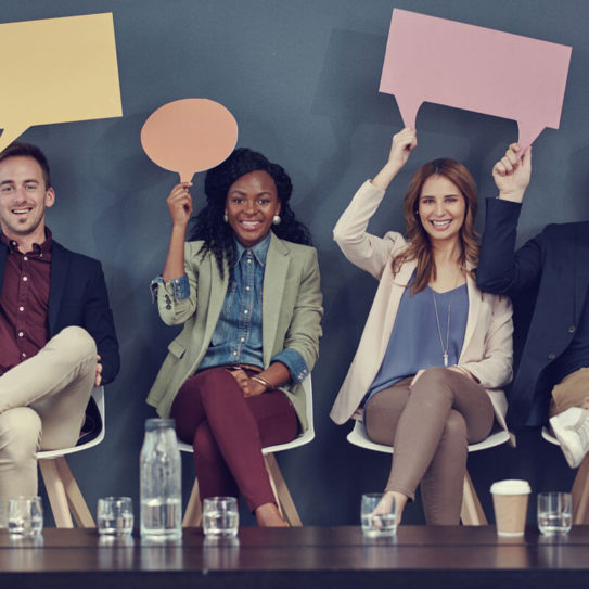 a group of young professionals hold paper cutouts of speech bubbles over their heads