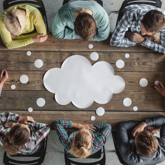 a group of young professionals sit around a table that has a paper speech bubble on it