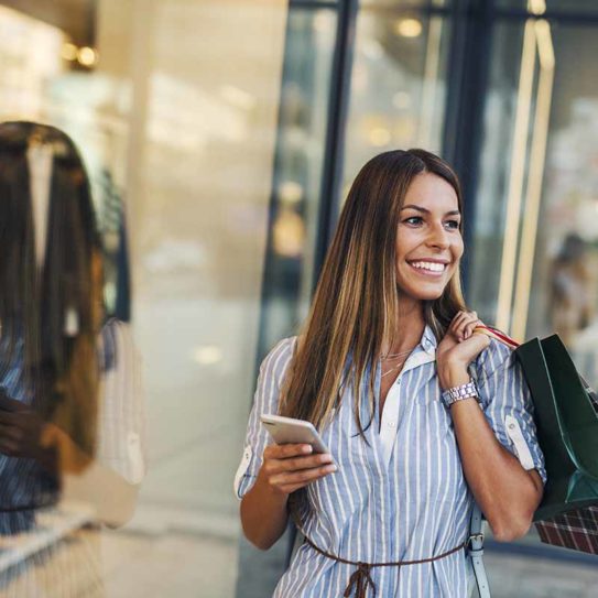 Woman checking smart phone in front of store window