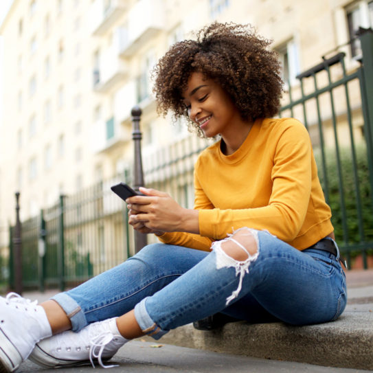 young woman sitting outside on street using her phone