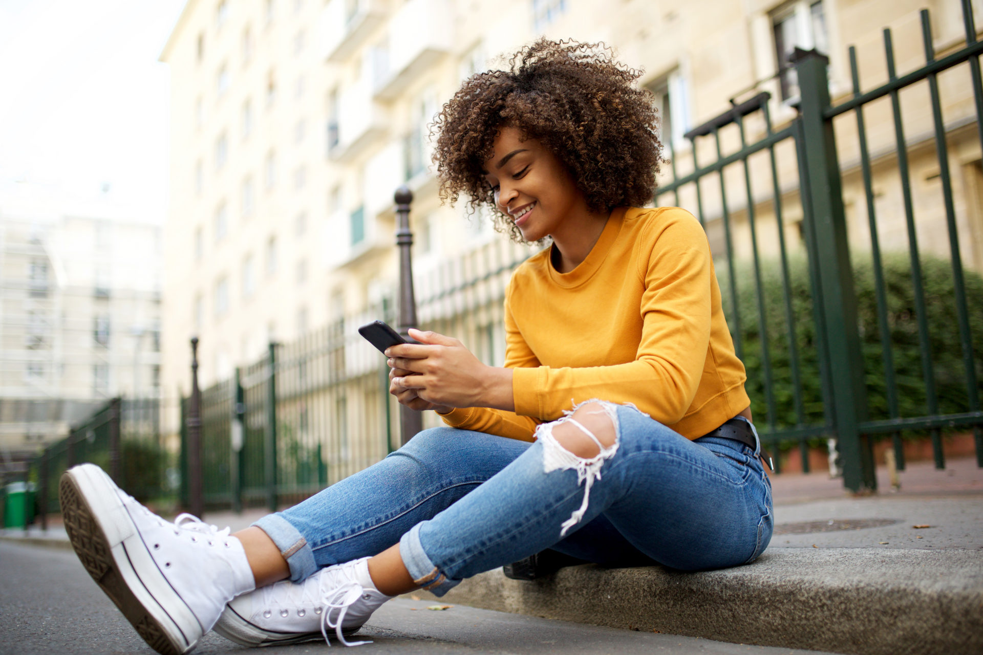 young woman sitting outside on street using her phone