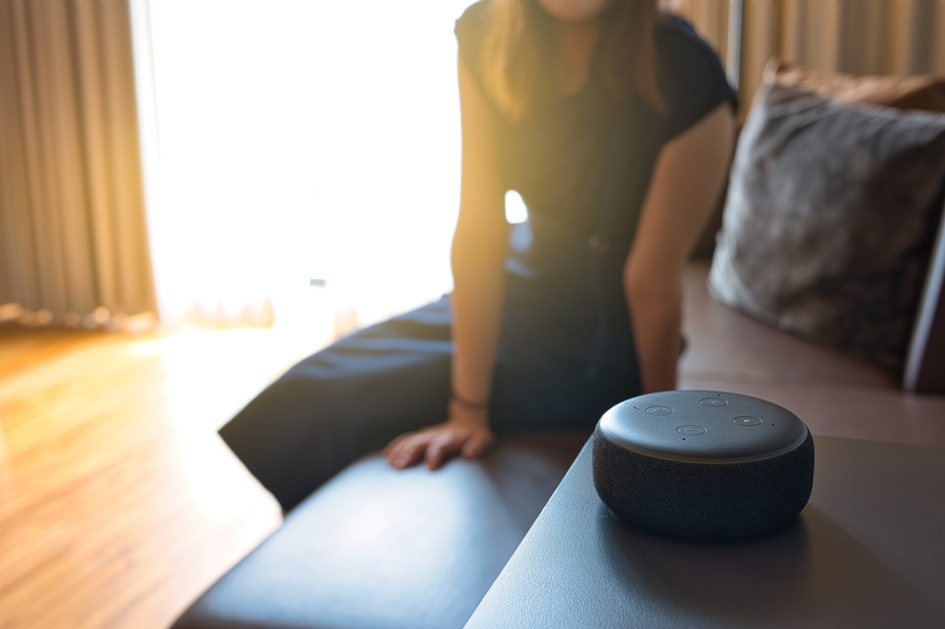 Woman sitting on a chair and talking to a speech recognition device, Amazon Alexa with sunlight background