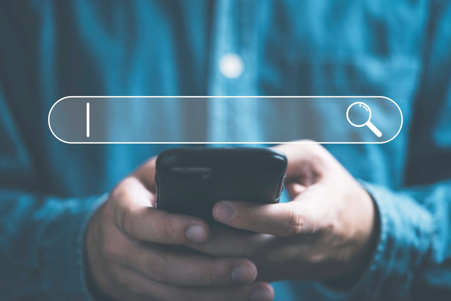 Closeup of a man holding a smartphone. A search bar is superimposed over the image to imply the man is on a search engine.