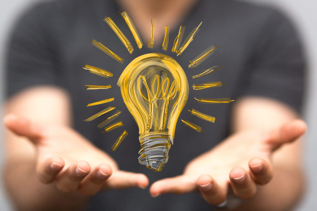Man in background with his hands stretched out to the camera. A drawn image of a lightbulb is superimposed over the image of the man to look like the lightbulb is hovering above his hands. Symbolizing SEO strategies for Google's AI Overview.