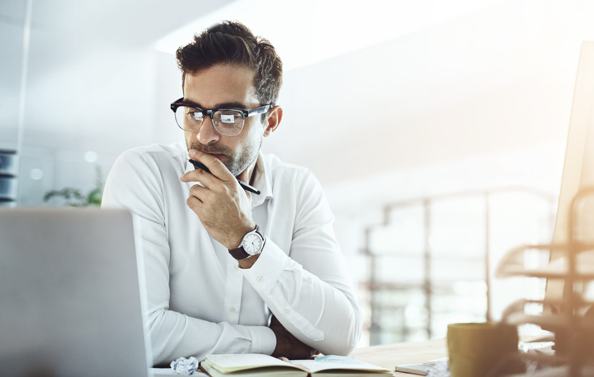 Image of a man in a white button-down shirt sitting in an office staring intently at his laptop screen, evaluating his company's performance with Google's AI Overview.