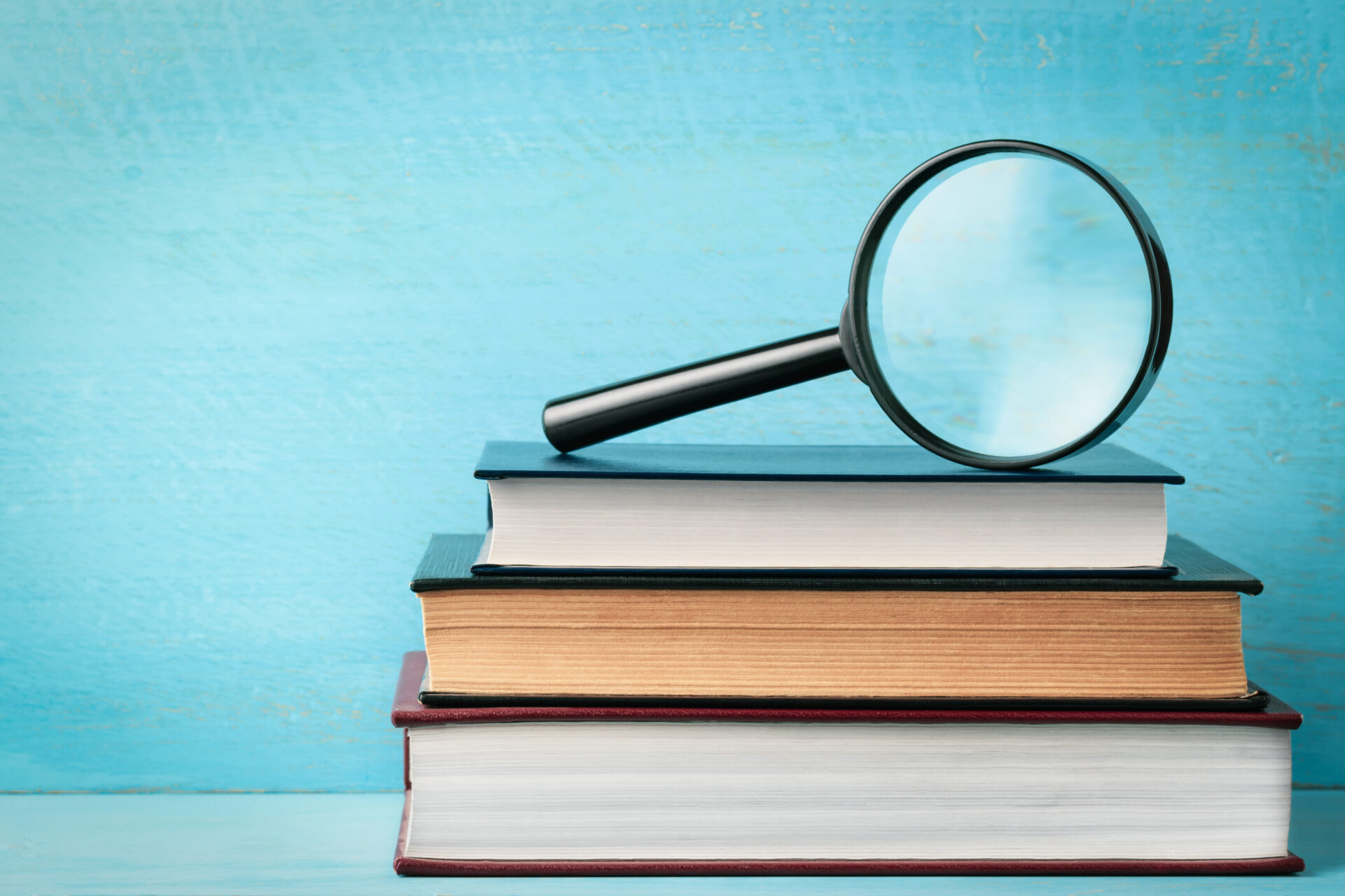 Three books stacked on one another with a magnifying glass propped on top. Symbolizing the glossary of digital marketing terms